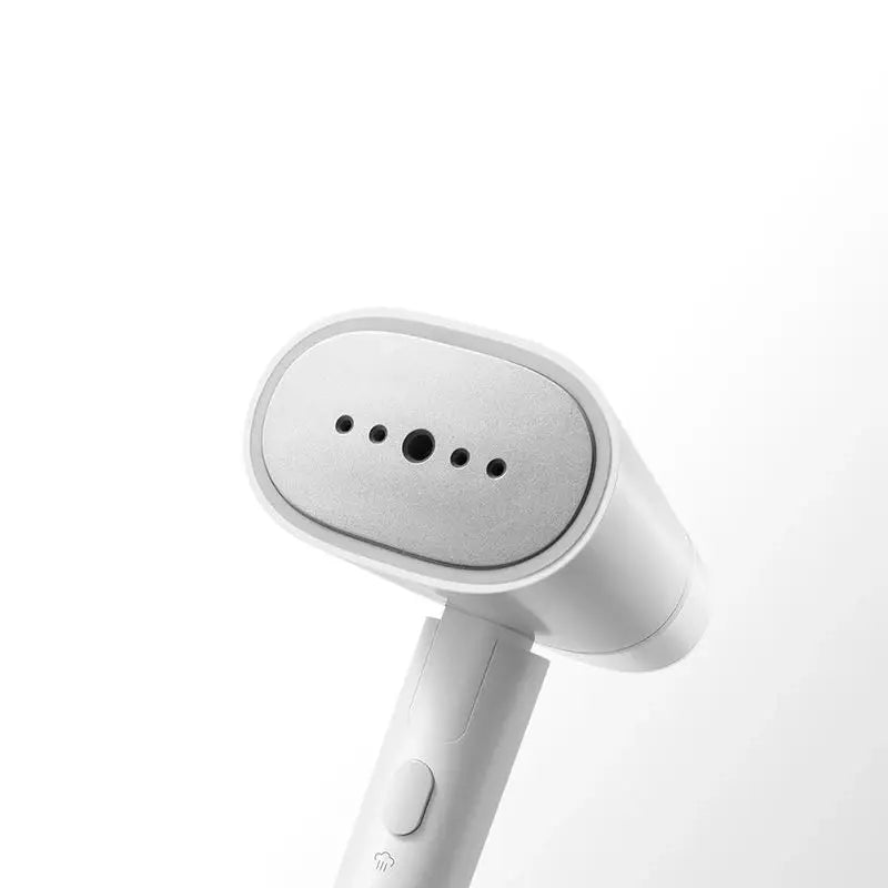 Handheld electric steam cleaner emitting fine hot mist onto a hanging shirt to remove wrinkles.